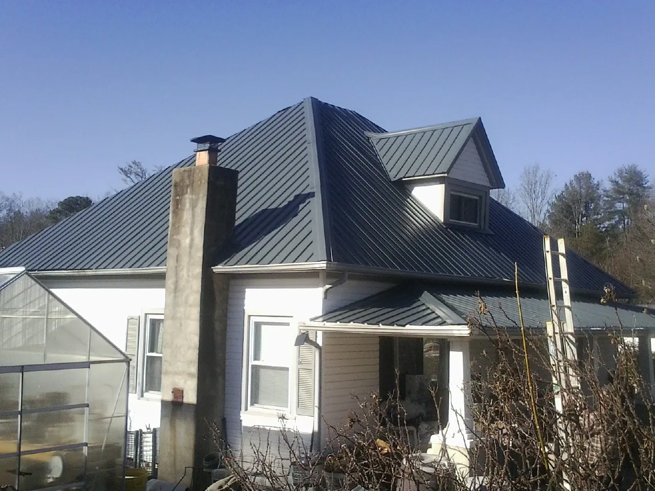 Dark blue standing seam metal roof on a white farmhouse with dormer — Slate & Tile Roof Repair by Roofing Brothers in Myerstown