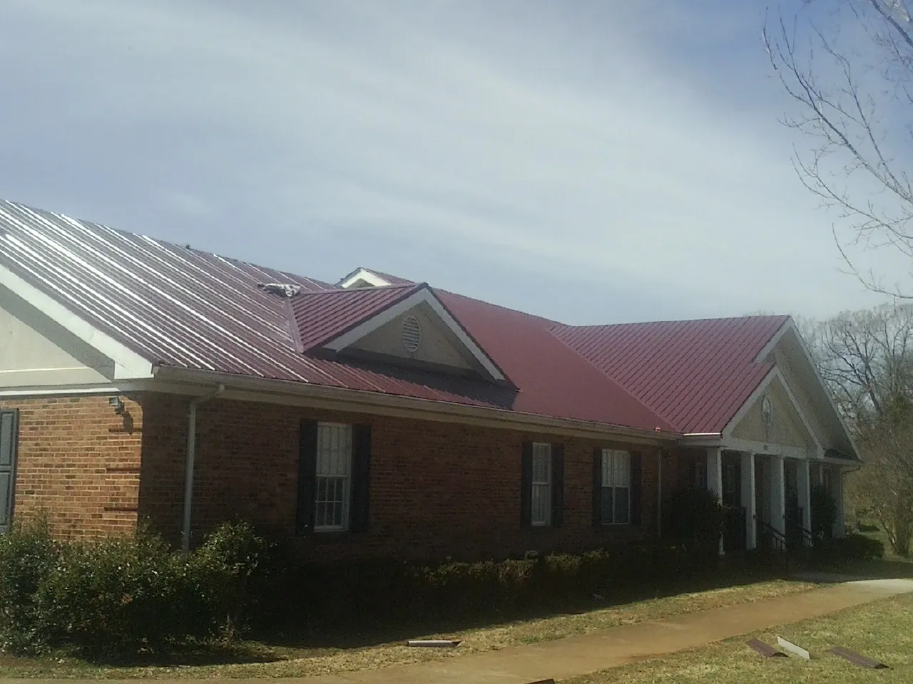 Red metal roof with gabled entries on a long brick building, from a Hail Damage Roof Repair job in Myerstown