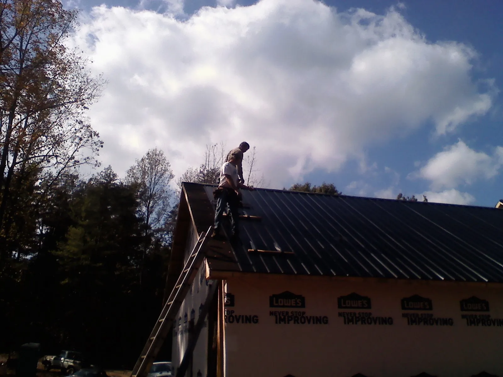 Roofer fastening dark metal panels high against a cloudy sky, from a Roof Inspection job in Myerstown