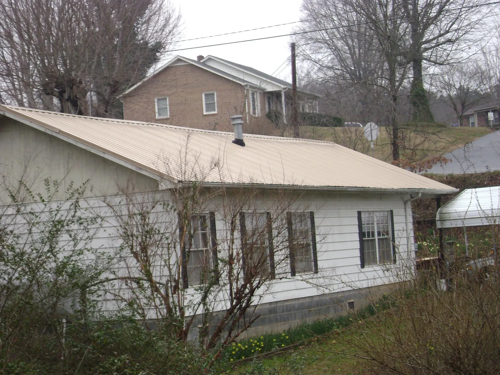 Tan metal roof on a white sided house set into a hillside — Commercial Roofing by Roofing Brothers in Myerstown